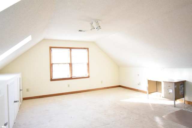 bonus room with visible vents, light carpet, a textured ceiling, vaulted ceiling with skylight, and baseboards