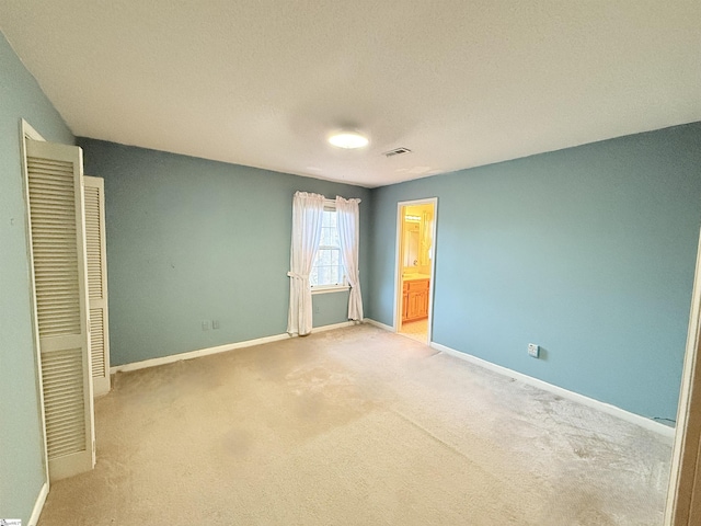 unfurnished bedroom with visible vents, baseboards, light colored carpet, and connected bathroom