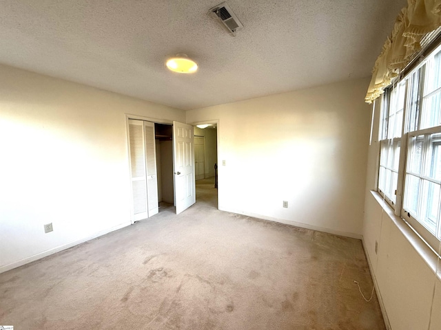 spare room featuring visible vents, light carpet, a textured ceiling, and baseboards