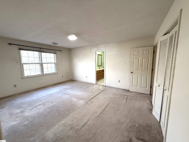 unfurnished bedroom with a closet, light carpet, a textured ceiling, and ensuite bath