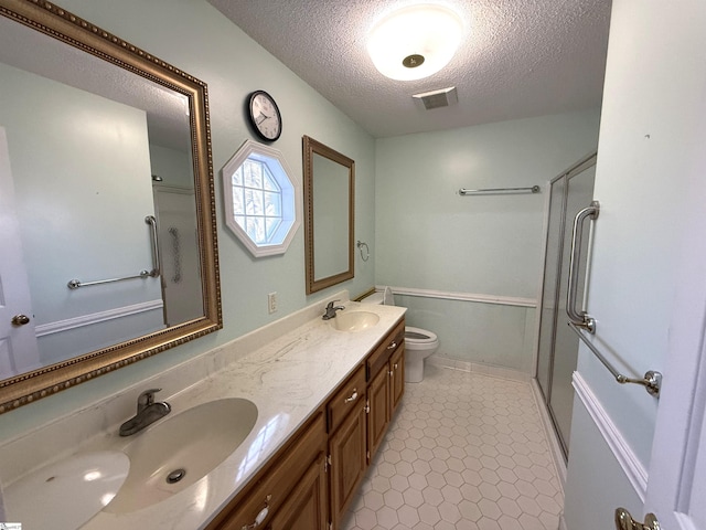 bathroom featuring a shower with shower door, visible vents, toilet, a sink, and a textured ceiling