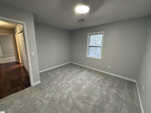 unfurnished room featuring dark colored carpet, visible vents, and baseboards