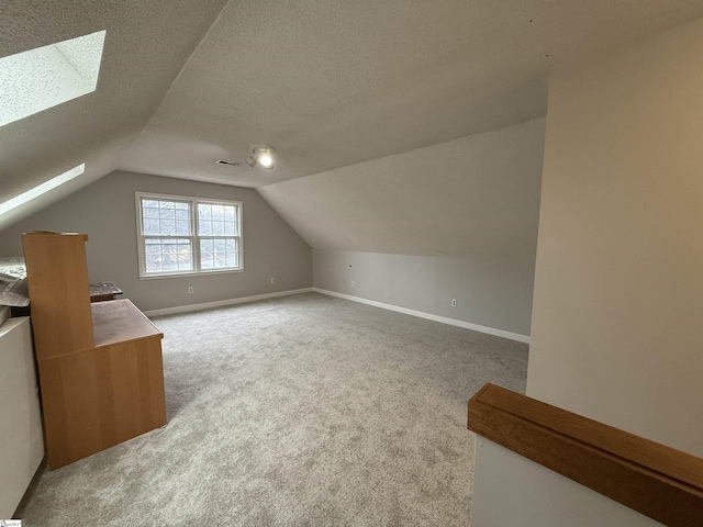 additional living space featuring visible vents, baseboards, a textured ceiling, lofted ceiling with skylight, and carpet flooring