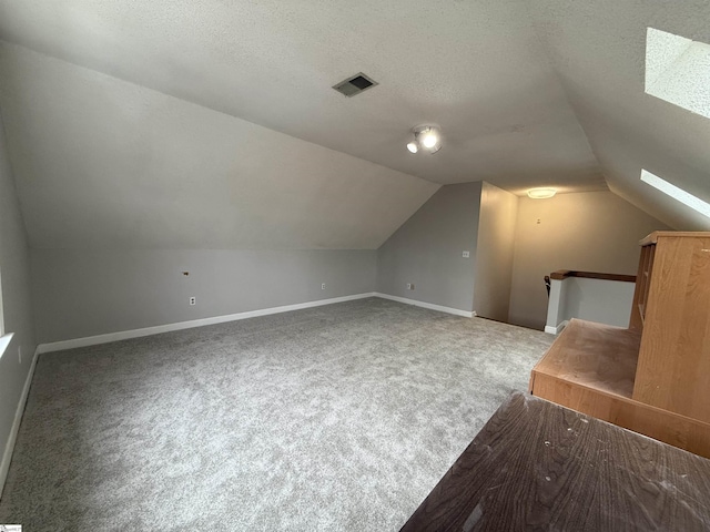 additional living space featuring baseboards, vaulted ceiling with skylight, a textured ceiling, and carpet