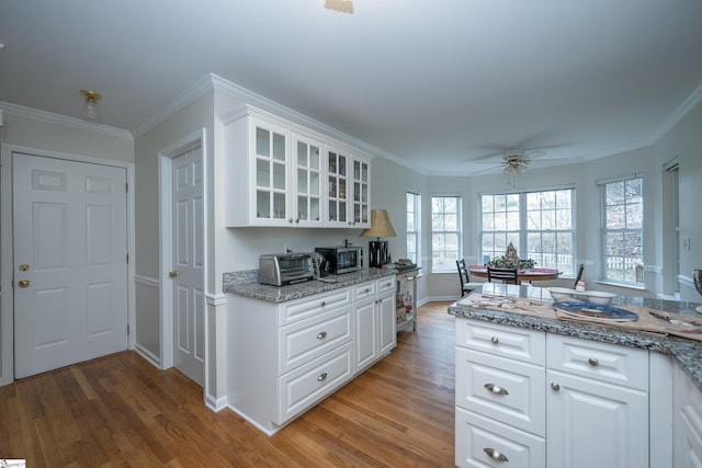 kitchen with white cabinetry, ceiling fan, light stone counters, crown molding, and hardwood / wood-style flooring