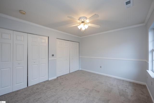 unfurnished bedroom with two closets, light colored carpet, ceiling fan, and crown molding