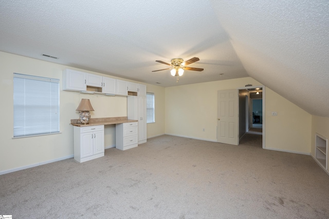 interior space featuring a textured ceiling, ceiling fan, light carpet, and vaulted ceiling