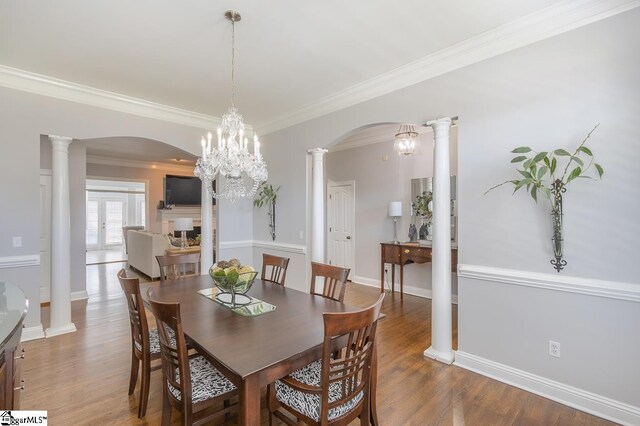 dining area featuring a notable chandelier, wood-type flooring, crown molding, and ornate columns