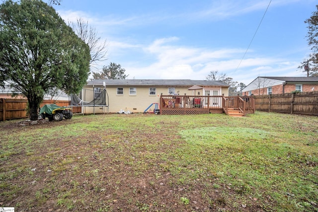 rear view of house featuring a yard, a deck, and a trampoline