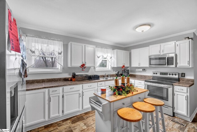 kitchen with a kitchen bar, crown molding, white cabinets, and stainless steel appliances