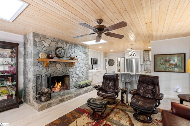 living room with ceiling fan, wood ceiling, light hardwood / wood-style flooring, and a stone fireplace