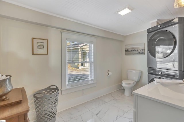 bathroom featuring stacked washer / drying machine, toilet, crown molding, and vanity