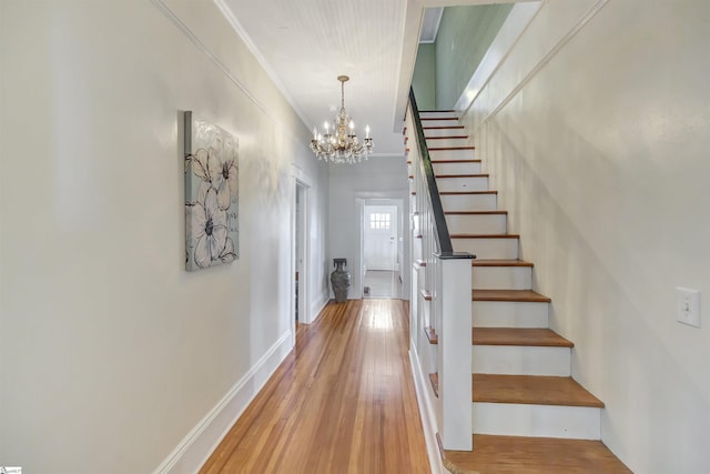 staircase with hardwood / wood-style floors, a notable chandelier, and ornamental molding