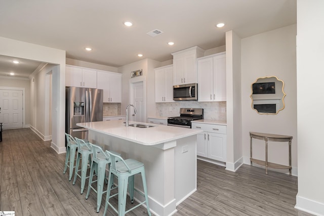 kitchen featuring appliances with stainless steel finishes, a kitchen island with sink, sink, light hardwood / wood-style flooring, and white cabinetry