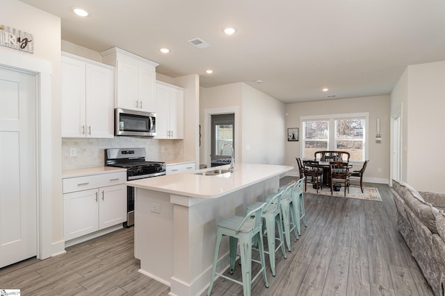 kitchen with white cabinets, appliances with stainless steel finishes, a center island with sink, and sink