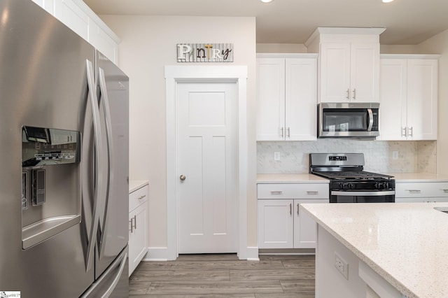 kitchen featuring white cabinetry, tasteful backsplash, light stone counters, light hardwood / wood-style flooring, and appliances with stainless steel finishes