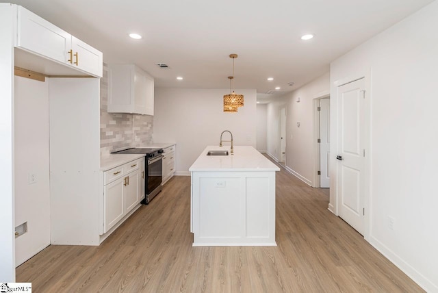 kitchen with stainless steel range with electric stovetop, pendant lighting, white cabinets, sink, and an island with sink