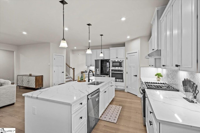 kitchen featuring pendant lighting, light wood-type flooring, an island with sink, appliances with stainless steel finishes, and white cabinetry