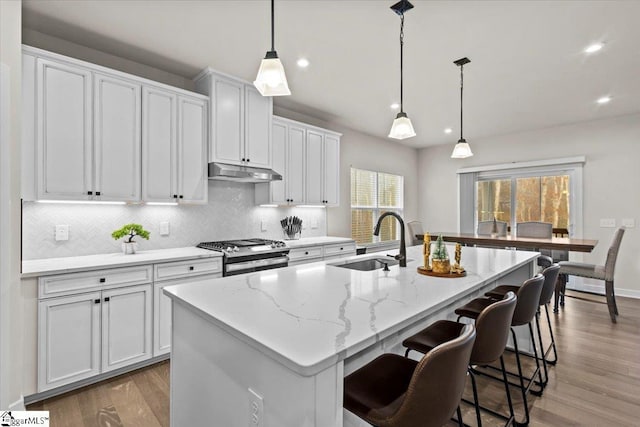 kitchen with pendant lighting, an island with sink, dark hardwood / wood-style flooring, white cabinetry, and stainless steel range with gas stovetop