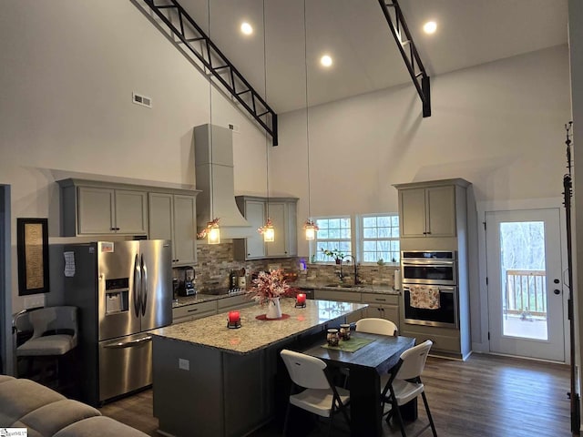 kitchen with a high ceiling, wall chimney range hood, sink, a kitchen island, and stainless steel appliances