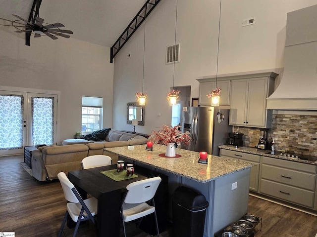 kitchen featuring hanging light fixtures, a high ceiling, stainless steel refrigerator with ice dispenser, black stovetop, and exhaust hood