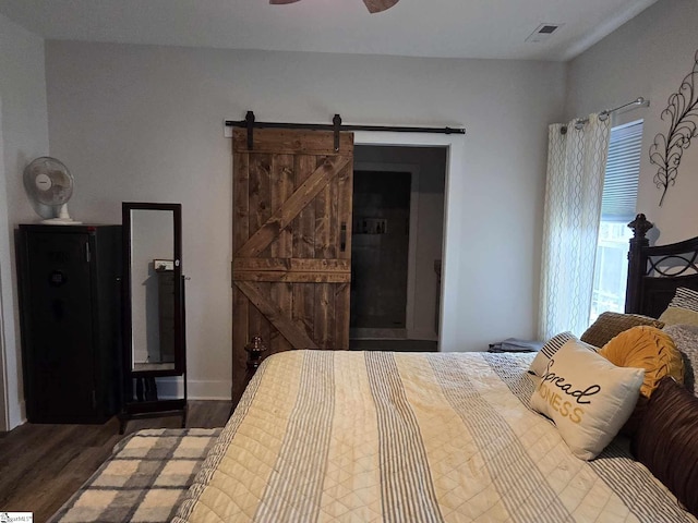 bedroom with a barn door, hardwood / wood-style flooring, multiple windows, and ceiling fan