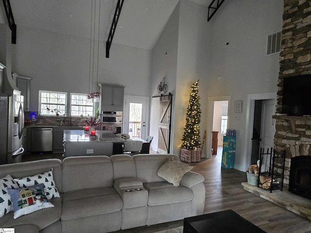 living room featuring high vaulted ceiling, a stone fireplace, sink, a barn door, and wood-type flooring