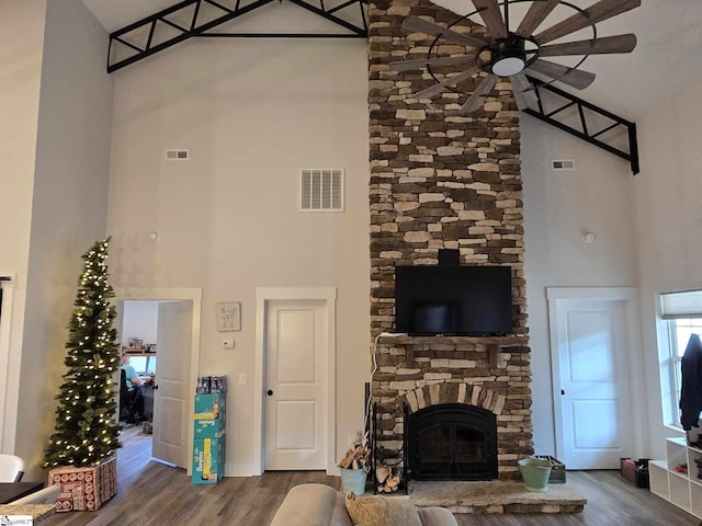 living room with hardwood / wood-style flooring, ceiling fan, a stone fireplace, and a towering ceiling