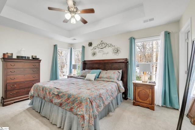 bedroom with ceiling fan, multiple windows, light carpet, and a tray ceiling