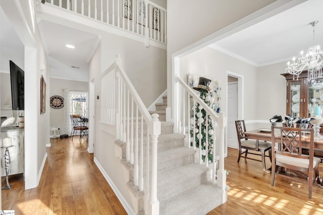 stairs featuring a towering ceiling, ornamental molding, a notable chandelier, and hardwood / wood-style flooring