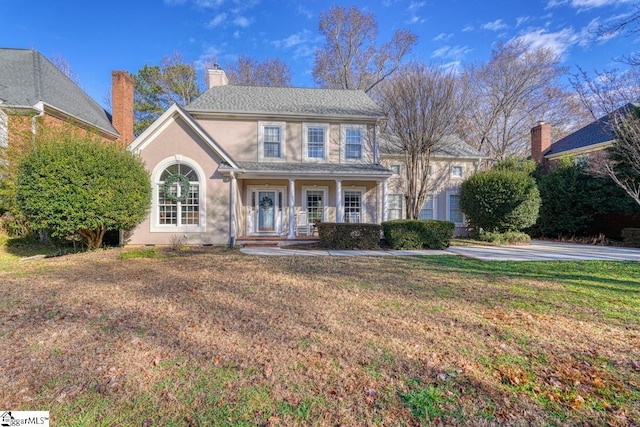 colonial inspired home featuring a porch and a front lawn