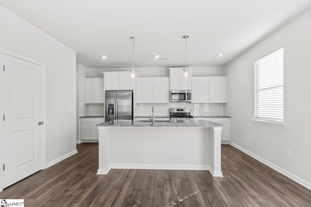 kitchen featuring light stone countertops, stainless steel appliances, white cabinetry, and a kitchen island with sink