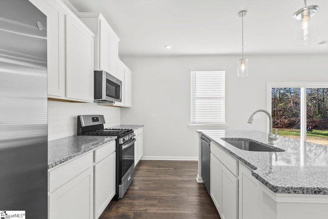 kitchen with appliances with stainless steel finishes, decorative light fixtures, white cabinets, light stone counters, and sink