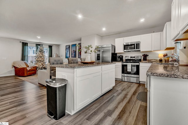 kitchen with stone counters, white cabinetry, stainless steel appliances, light hardwood / wood-style floors, and a kitchen island