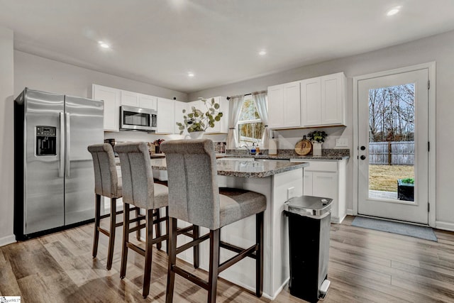 kitchen featuring a center island, a breakfast bar area, light wood-type flooring, white cabinetry, and stainless steel appliances