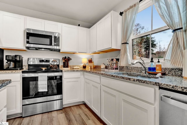 kitchen featuring sink, light stone counters, light hardwood / wood-style flooring, white cabinets, and appliances with stainless steel finishes