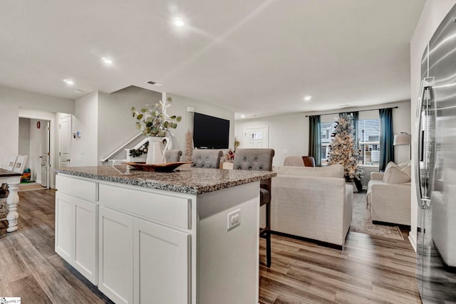 kitchen featuring stainless steel fridge, a kitchen island, light hardwood / wood-style flooring, stone counters, and white cabinetry