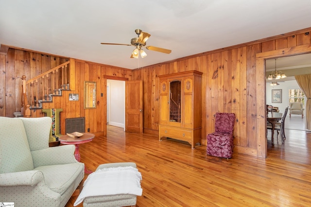 living room featuring wooden walls, ceiling fan with notable chandelier, hardwood / wood-style flooring, and crown molding