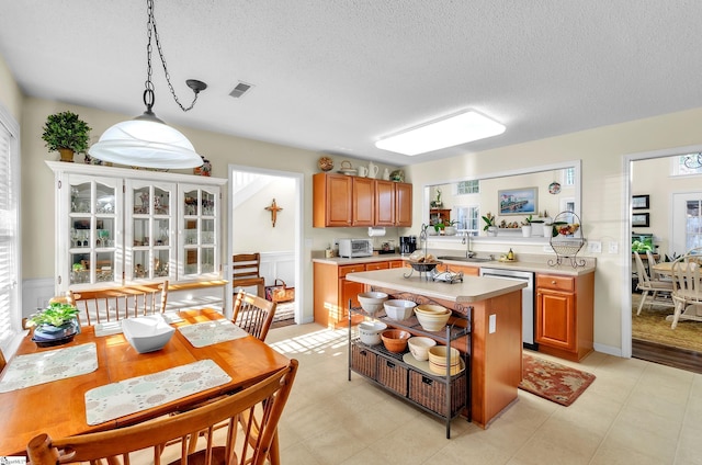 kitchen with dishwasher, a center island, sink, a textured ceiling, and decorative light fixtures