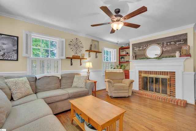 living room with a brick fireplace, light hardwood / wood-style flooring, ceiling fan, and crown molding