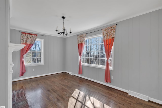 empty room featuring ornamental molding, dark wood-type flooring, and an inviting chandelier