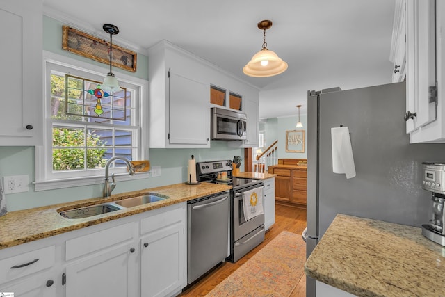 kitchen with white cabinets, sink, hanging light fixtures, appliances with stainless steel finishes, and light hardwood / wood-style floors