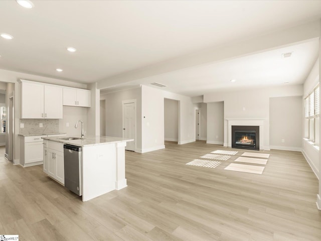 kitchen featuring a center island with sink, tasteful backsplash, stainless steel dishwasher, white cabinets, and sink