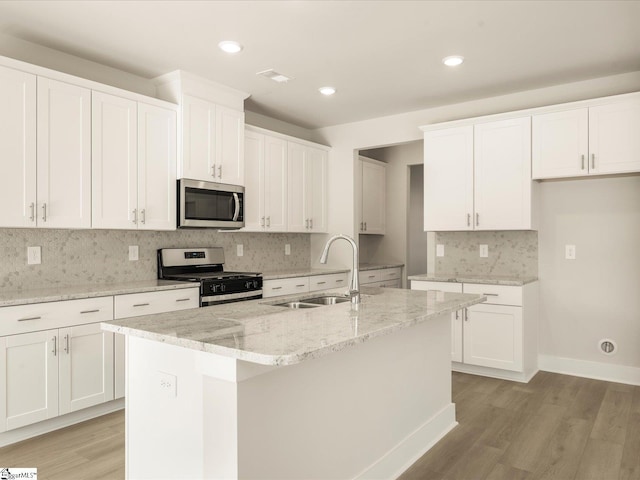 kitchen with stainless steel appliances, white cabinets, a center island with sink, and sink