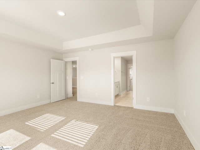 unfurnished bedroom with connected bathroom, a tray ceiling, and light carpet