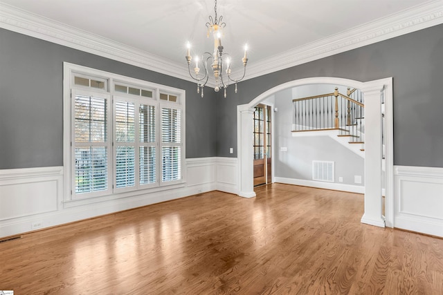 unfurnished dining area featuring hardwood / wood-style floors, decorative columns, an inviting chandelier, and ornamental molding