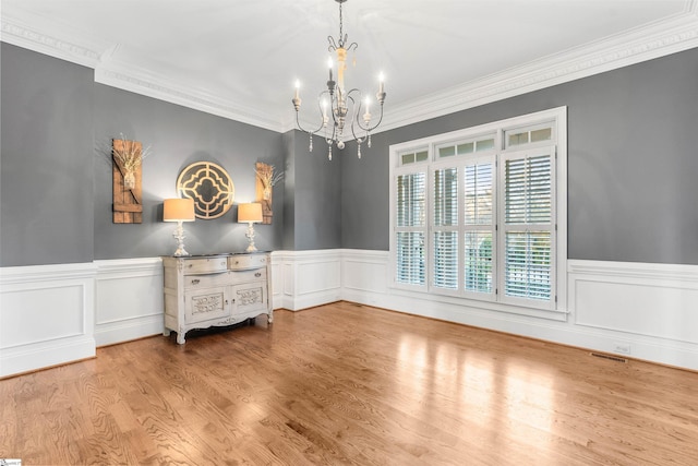 spare room featuring light wood-type flooring, crown molding, and a chandelier