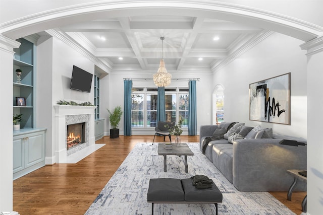 living room with crown molding, hardwood / wood-style flooring, a fireplace, beam ceiling, and a chandelier