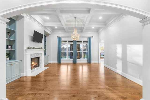 unfurnished living room featuring beamed ceiling, wood-type flooring, a fireplace, and an inviting chandelier