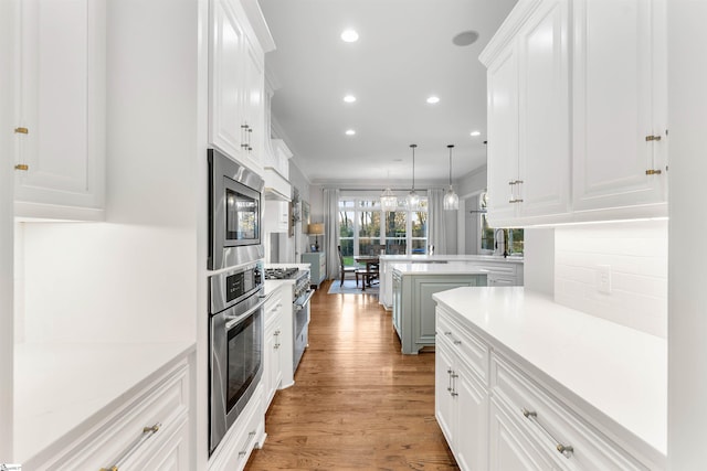 kitchen featuring hanging light fixtures, stainless steel appliances, kitchen peninsula, white cabinets, and light wood-type flooring